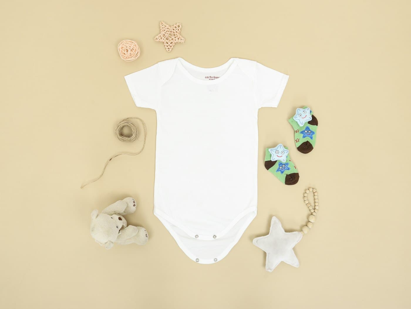 White baby bodysuit flat lay with star-print socks on a cream background