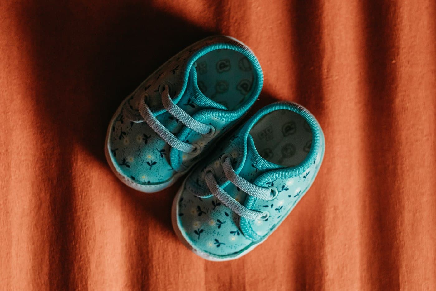 Teal floral baby sneakers viewed from above on terracotta fabric